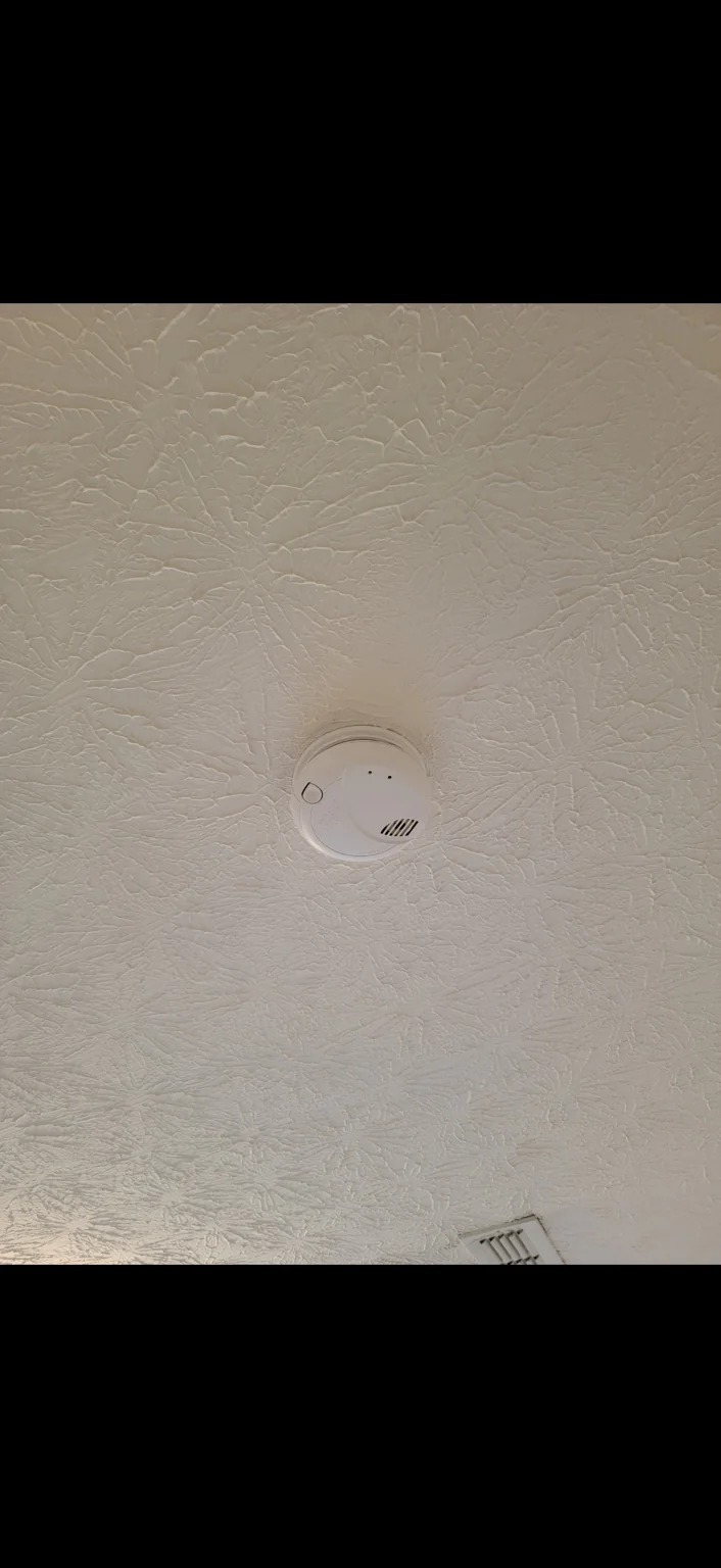 Updated smoke alarm. A newer smoke alarm mounted on a textured ceiling.